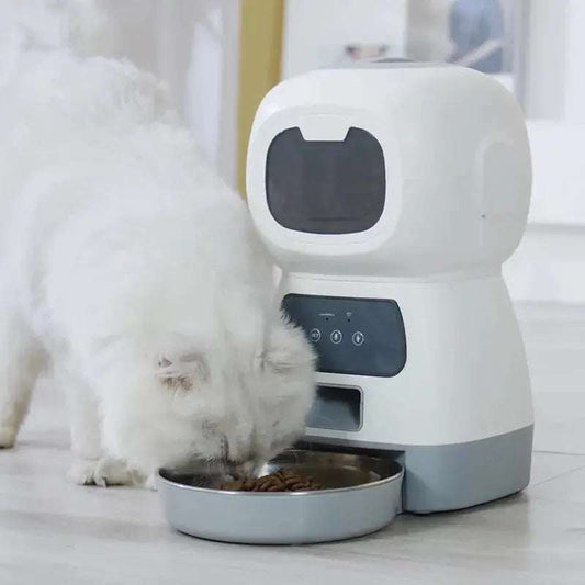 White automatic pet feeder dispensing food to a cat from a stainless steel bowl on a light floor